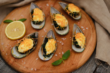 Mussels baked with spinach and Parmesan cheese with lemon and mint on a wooden desk