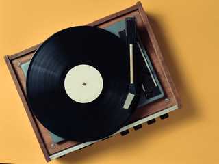 Vintage vinyl turntable with vinyl plate on a yellow pastel background. Entertainment 70s. Listen...