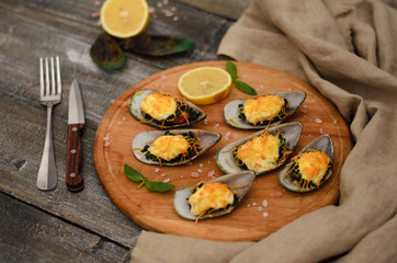 Mussels baked with spinach and Parmesan cheese with lemon and mint on a wooden desk
