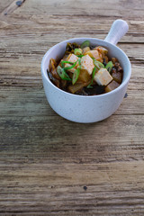 Korean kimchi stew with tofu served in a claypot with a handle. Wooden background, copy space 