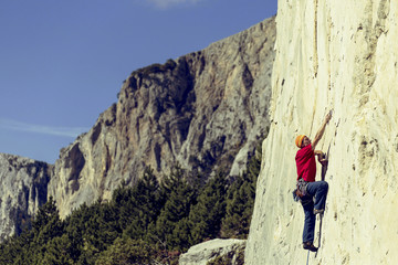 Young man climbs on a rocky wall in a valley with mountains.
