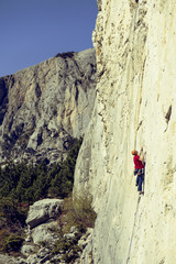 Young man climbs on a rocky wall in a valley with mountains.