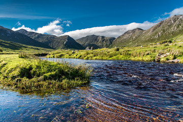 Connemara landscape in Ireland: a river flows amid the meadows in front of the majestic Twelve Bens mountains
