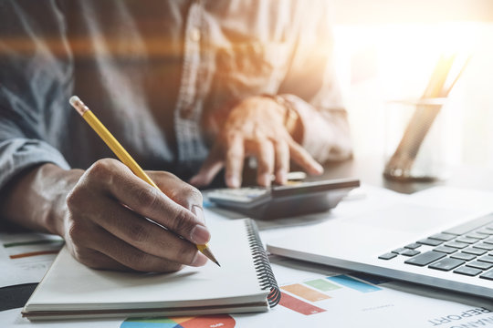 Businessman with calculator and laptop computer counting with cost and writing make notes at office, Business financial concept