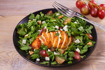 Chicken, grapes and goat cheese salad in black plate on wooden background