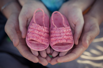 Woman and man father and mother young hands only isolated holding little baby pink shoes in emotional love heart pose.Future family happyness