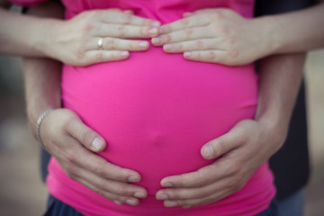 Pretty young pregnant lady woman with huge beautifull green eyes and pout red lips wearing dark pink dress with blue skirt holding hands on her tummy awaiting miracle with bouquet of lavander flowers.