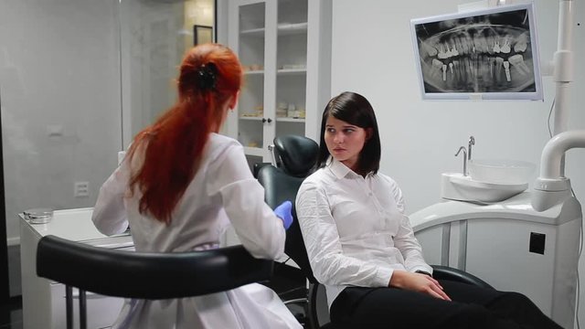 Beautiful girl consulted a dentist in his office ball on the thymus of the pain pointing to her teeth. White, sterile doctor's office. The screen shows an x-ray of the tooth in the oral cavity