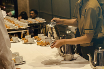 The waitress is making coffee on a white coffee mug with sausage between the brake and the brake background.