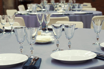 Preparation for a wedding banquet. The tables are covered with lilac tablecloth. Wine glasses are on the tables in the restaurant.