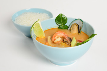 Traditional Thai soup with seafood, mushrooms and coconut milk in a bowl with rice on white background