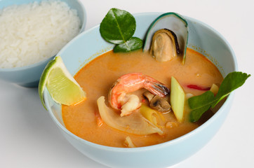 Traditional Thai soup with seafood, mushrooms and coconut milk in a bowl with rice on white background