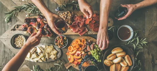 Tuinposter Flat-lay of friends hands eating and drinking together. Top view of people having party, gathering, celebrating together at wooden rustic table set with different wine snacks and fingerfoods © sonyakamoz