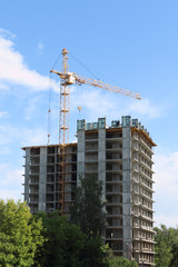 Fototapeta na wymiar Tall crane works near tall residential building on construction site at summer day