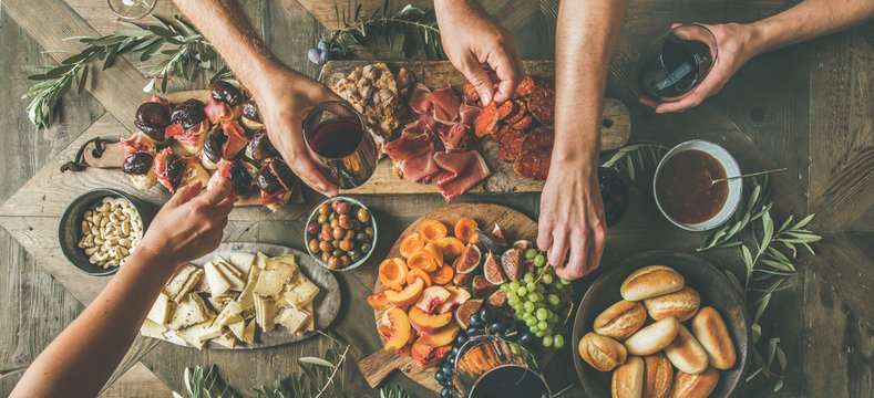 Fototapeta Flat-lay of friends hands eating and drinking together. Top view of people having party, gathering, celebrating together at wooden rustic table set with different wine snacks and fingerfoods