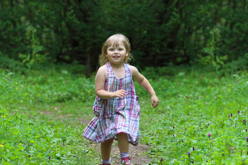 Smiling little blonde girl in dress runs at summer day in green park