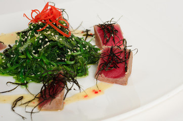 Fresh tuna salad with wakame seaweed and sesame seeds on a plate isolated on white background