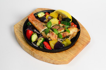 Red snapper baked with vegetables in a pan on a wooden desk