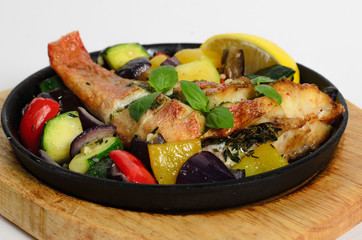 Red snapper baked with vegetables in a pan on a wooden desk