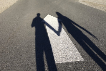 Shadow of couple holding hands on the sunny asphalt road with painted big white arrow on the floor.
