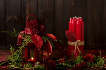 Still life on a dark background. Decor of candles and candlesticks with juniper, daisies and red leaves.