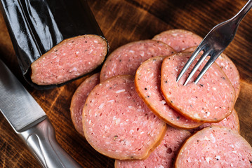 Pile of delicious smoked sausage sliced on a burnt wooden cutting board with part of knife and fork visible at the side.