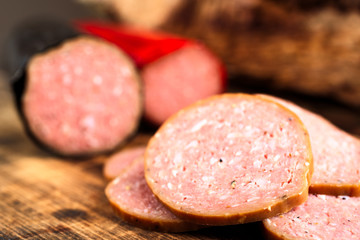 Closeup of delicious smoked sausage sliced on a burnt wooden cutting board. Shallow focus on front slice. Sausages blurred in background.