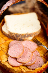 Pile of delicious smoked sausage with bread and a fork on a birch bark tray.