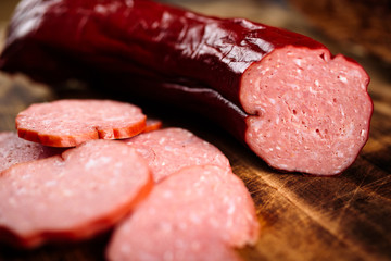 Handmade delicious smoked sausage on burnt wooden cutting board with pile of slices.