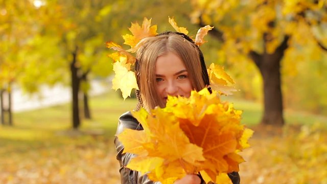 Young girl enjoying autumn in the park. she holding a bouquet of autumn leaves in her hands