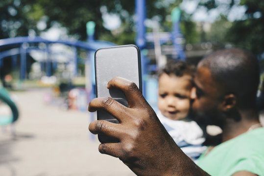 Father taking selfie through smart phone while kissing son at park