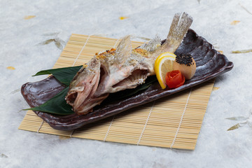 Salt-Grilled Snapper (Shioyaki) served with sliced lemon and tomato on stone plate on makisu (Meal...