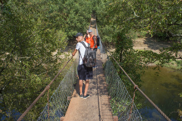 Obraz premium Trekking together. Active hikers. Travelers travel on the artificial roadway of the suspension bridge