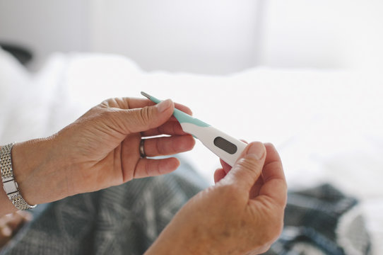 Cropped image of senior woman examining thermometer at home