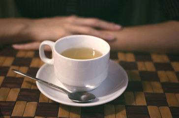 Cup of tea with spoon on the dish and woman's hands on the cafe table. Tea time.