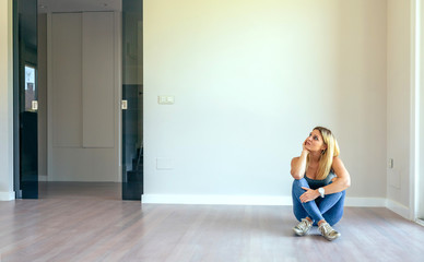 Obraz premium Thoughtful blonde girl sitting in a empty living room