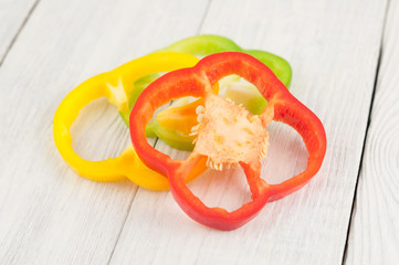 Three slices of colored red and green and yellow fresh ripe raw pepper on old rural white wooden planks
