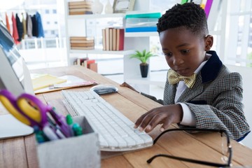Boy imitating as businessman using computer at desk - obrazy, fototapety, plakaty