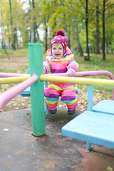 Fototapeta na wymiar 1 years little girl riding on the carousel in autumn outdoors