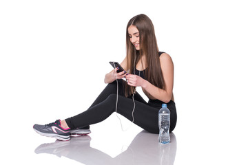 Fototapeta premium Portrait of a young athlete woman listening to music with earphones over white background. Attractive fitness girl chatting on smartphone ion studio.