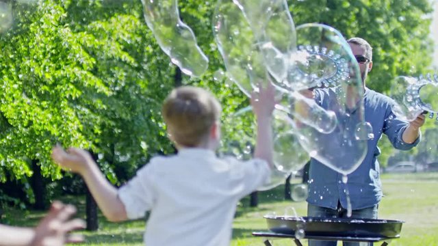 Kids catching large and small bubbles in the air while professional bubble artist making show with two wands at warm summer day in park