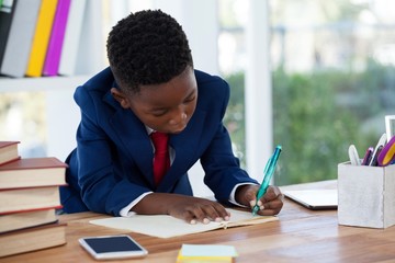 Boy imitating as businessman writing on diary - obrazy, fototapety, plakaty