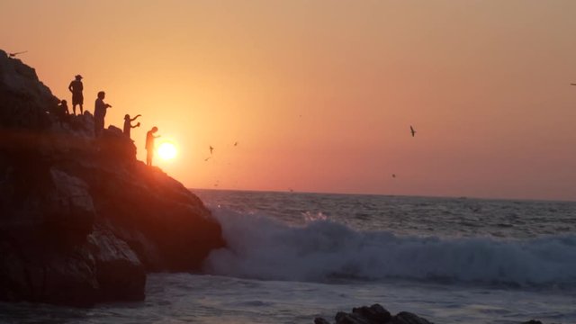 panoram rock coast with  figure of fishermans on the cliff at sunset, red sun on horizon