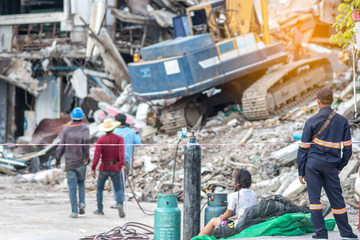 Worker controlling backhoe demolishing old buildings. Workers at demolition site with pile of rubble and bulldozer at Bangkok site.