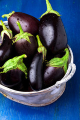Fresh eggplant in grey basket on blue wooden table.Rustic background. Close up. Vegan vegetable.