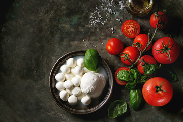 Ingredients for italian caprese salad. Mozzarella balls, buffalo in metal vintage plate, tomatoes, basil leaves, olive oil with vinegar over dark background. Top view with space. Rustic style