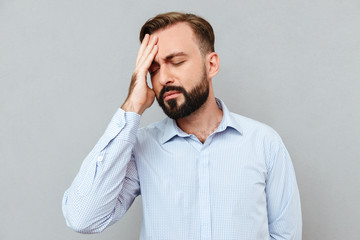 Bearded man in business clothes having headache and touching his forehead