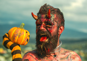 Halloween devil man holding pumpkin in striped sock