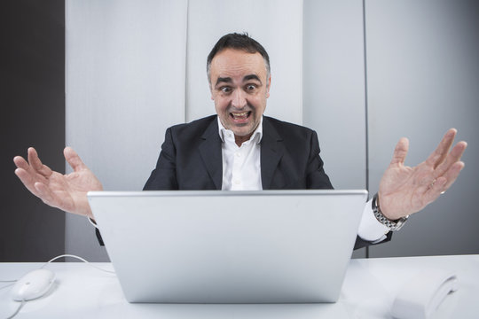 Uomo d'affari davanti al suo computer guarda perplesso con le mani sollevate