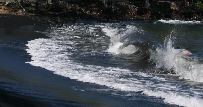 Boy body surfing black sand beach Hawaii. Tropical wonderland. Big Island, largest, most volcanic active location. Economy is tourism based. Water and tropical beach recreation and fun.